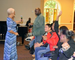 Executive Director Myrna Clayton hands microphone to audience member to all him an opportunity to sing and showcase his talent.