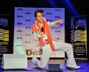 DELVIS (teen singer and Elvis Entity) gets down on one knee and points to the audience as he sings an Elvis Presley song.
