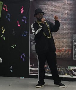 Young adult male with a developmental disability wearing hip hop attire and a large gold chain performs as a rapper.