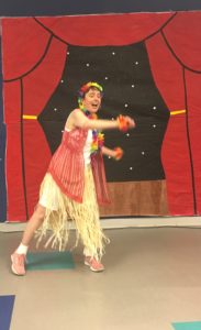 Young adult female with a developmental disability dances in a Hawaiian hula costume.
